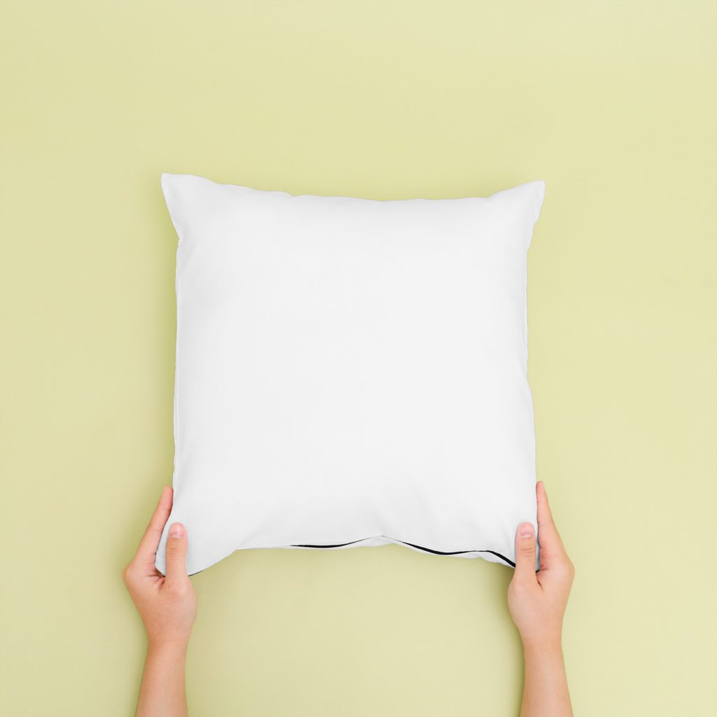 Woman's hands hold a pillow on a yellow background.