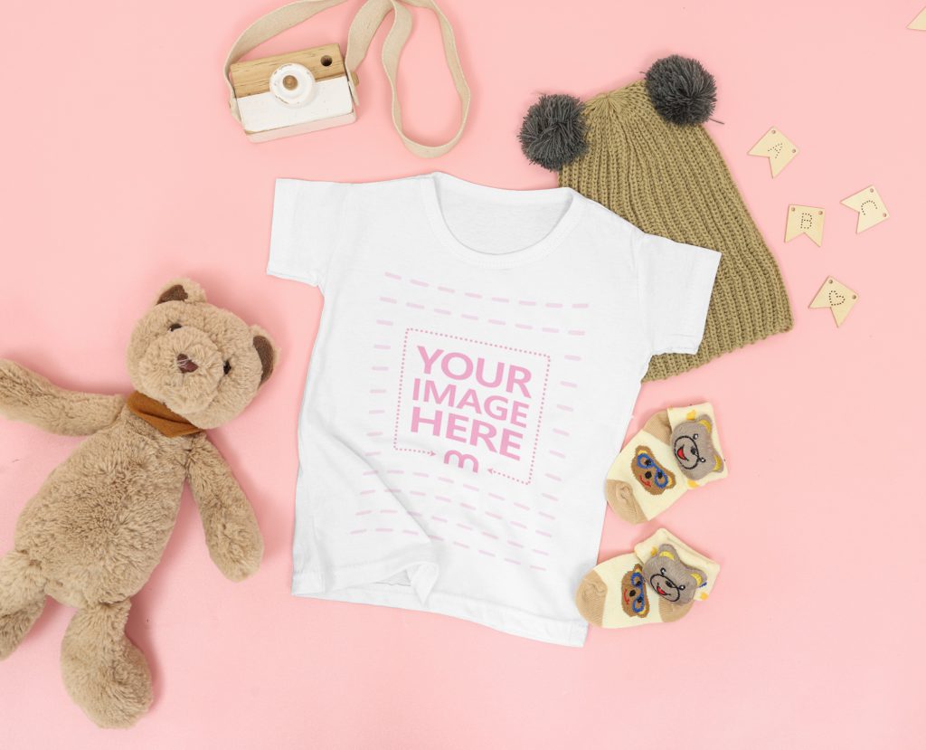 baby shirt on a pink background. with teddy bear, bear socks, hat and toy camera