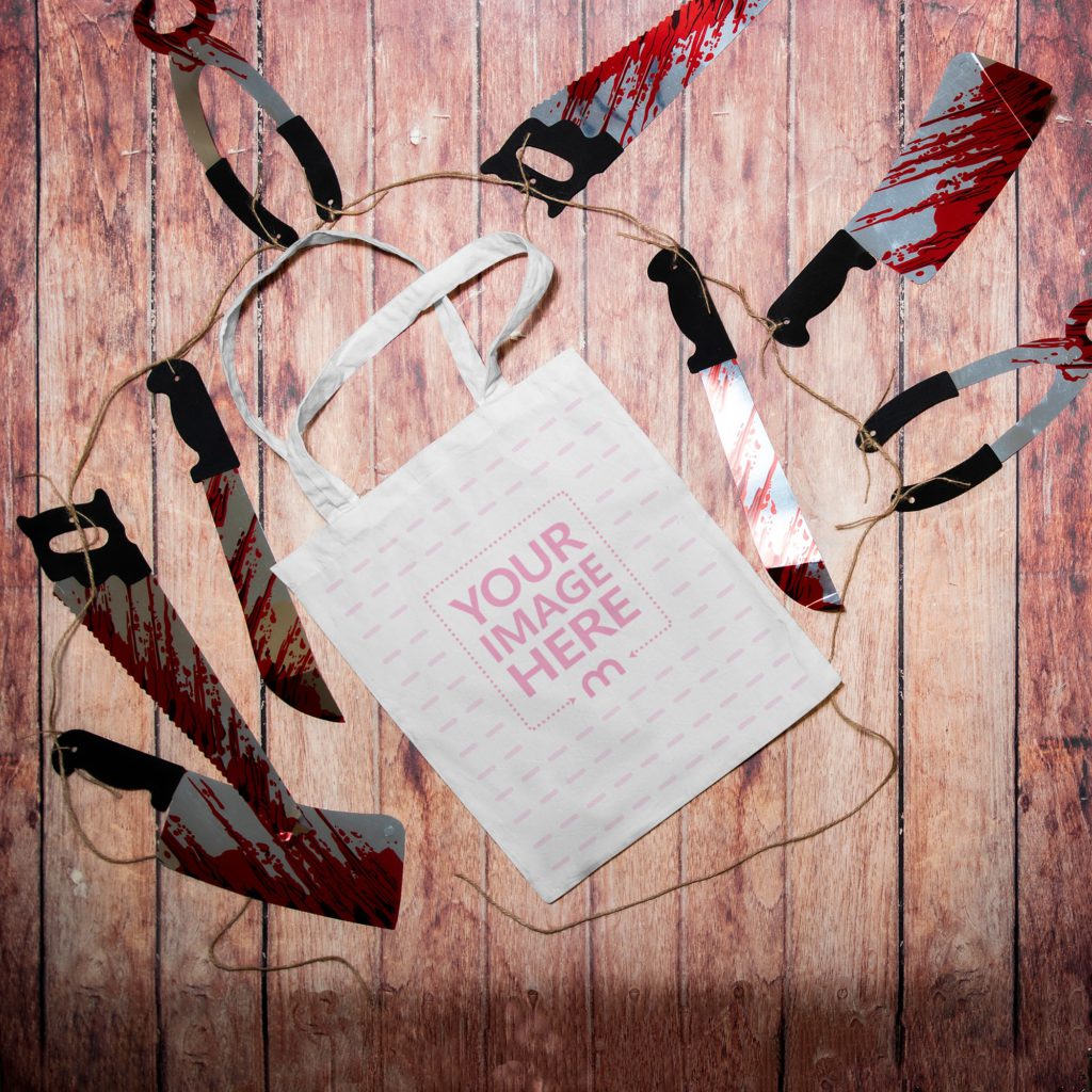 Tote bag on a wooden background. Next to the bag are bloody knives and saws.