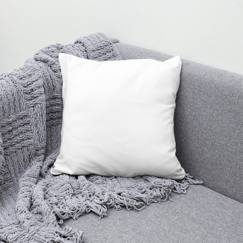 A pillow on a gray sofa with a knitted blanket.