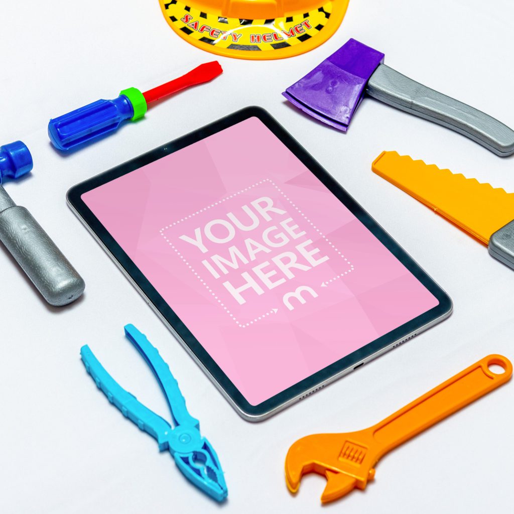 IPad on white background with game tools, hammer, saw, screwdriver, pliers and helmet.