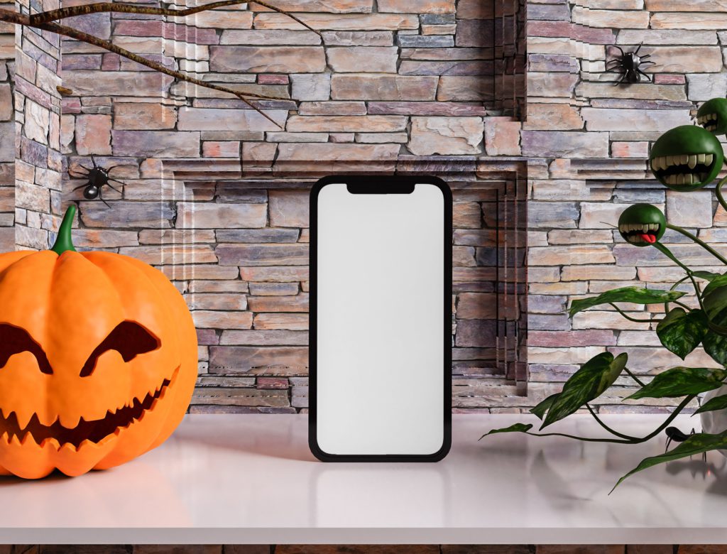iphone on a white table, stone background behind. next to it is a pumpkin, a scary plant and spiders
