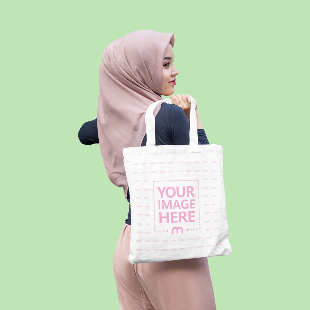 Muslim woman poses with tote bag in studio. He has a Tote Bag on his back. The woman is smiling and confident.
