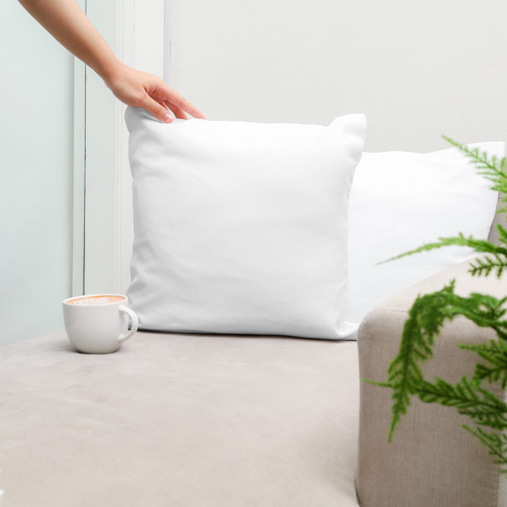 Cushions on a light gray sofa, with a cup of coffee. There is a plant next to the sofa.