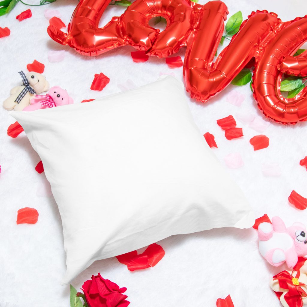 A pillow on a white furry background. There are rose flowers, teddy bears and a love balloon all around.