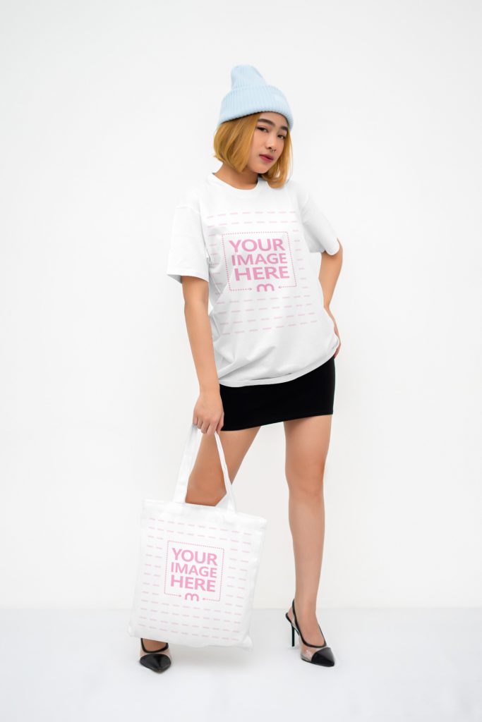 A woman poses in the studio with a tote bag. The woman is wearing a black skirt, a shirt and a hat.